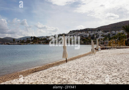 View of empty beach, closed sun shades (umbrellas), white summer houses and landscape in Turkbuku village on Bodrum peninsula in autumn. The image als Stock Photo