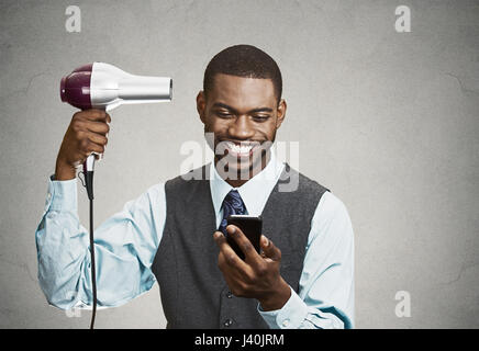 Closeup portrait happy, smiling business man, deal maker reading good news on smart, mobile phone, holding hairdryer isolated black grey background. H Stock Photo