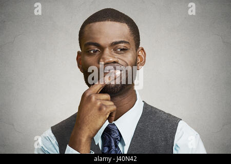 Closeup portrait young, puzzled business man thinking, deciding deeply something, finger on lips looking confused, unsure isolated grey wall backgroun Stock Photo