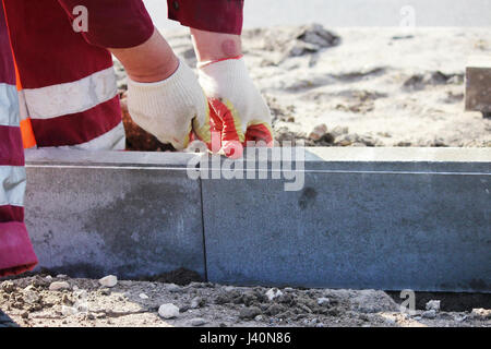 Repair of the sidewalk. Professional working masons in overalls lay curbs before laying stone paving slabs. Stock Photo