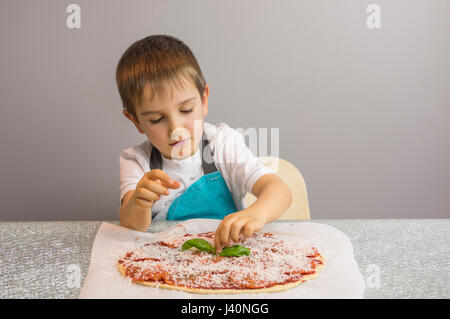 Little boy is making pizza, finishing with basil leafs Stock Photo