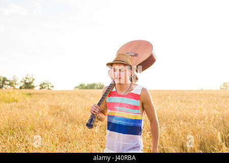 Musician holding acoustic guitar and walking in summer fields Stock Photo