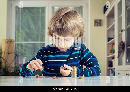 Little boy playing with coins making stacks. Learning financial responsibility and planning savings concept. Stock Photo