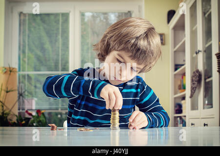 Little boy making stack of coins, counting money at table. Learning financial responsibility and planning savings concept. Stock Photo