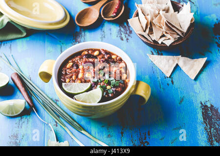 Chili con carne stew served in yellow bowl on rustic blue wooden table, Mexican cuisine, pastel retro tones Stock Photo