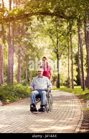 smiling daughter in the park pushing enjoying senior man in wheelchair Stock Photo