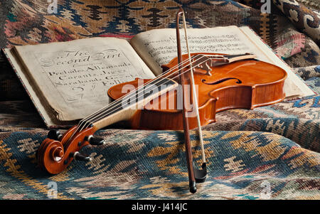 Baroque violin and bow & 18th century print of Corelli's Op 5 on Persian kilim. Focus-stacked still life in natural window light, trompe l'oeil effect Stock Photo