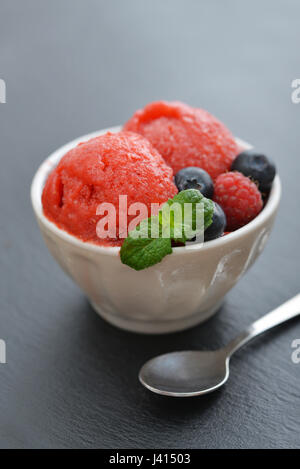 Fruit strawberry sorbet with raspberry, blueberry and mint in a bowl on black slate background Stock Photo