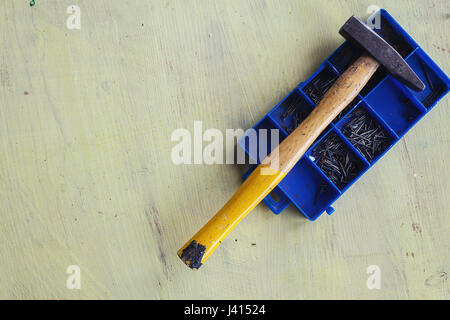 One old used hammer on box of nails on wooden plank painted in pale yellow. Stock Photo