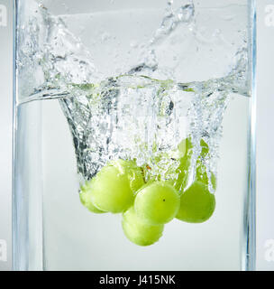 Fresh green grapes splashing into water. Stock Photo