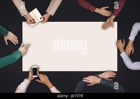 Teamwork and cooperation concept - top view of six people drawing or writing on a large white blank sheet of paper on blackboard. Stock Photo