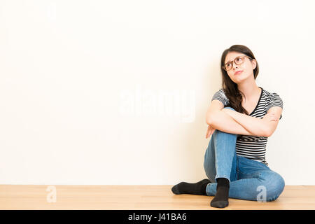 lovely confused student woman thinks and dreaming with casual clothing sitting on wooden floor over blank copy space white wall background.