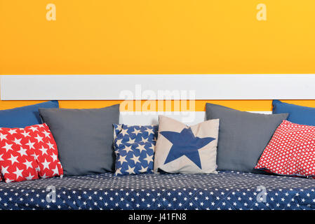 Children's bed with different color pillows against orange wall in the room Stock Photo