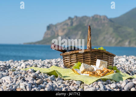 Picnic basket with wine, cheese and grapes on a sea beach Stock Photo