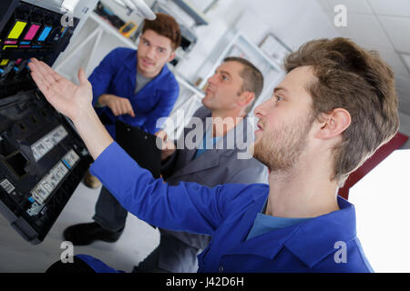 Three men looking at ink cartridges in photocopier Stock Photo