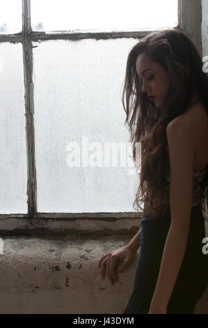 Sad young woman standing by the window Stock Photo