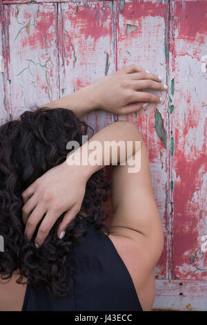 Rear view of a young woman with black curly hair leaning against an old door Stock Photo