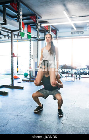 Man carrying woman on his shoulders, doing squats. Stock Photo