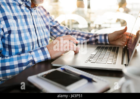 Unrecognizable senior businessman working on laptop in cafe Stock Photo