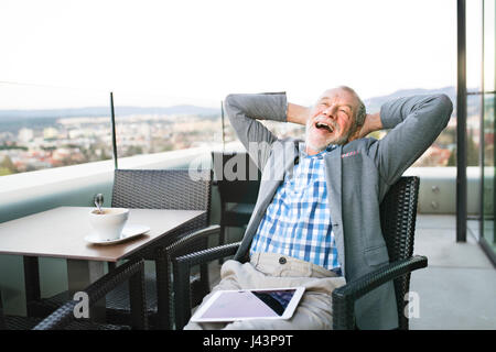 Senior businessman with a tablet in rooftop cafe Stock Photo