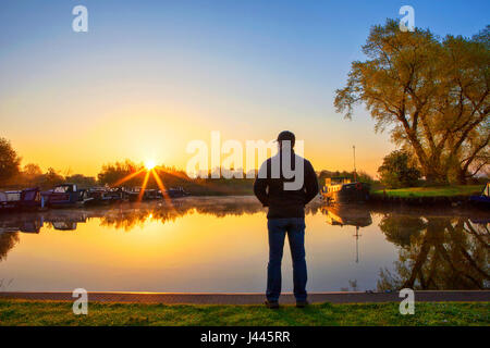 Rufford, Lancashire, 10th May 2017. UK Weather.  A man watches a beautiful sunrise & early morning mist as the sun rises above the canal boats moored on Rufford Marina in Lancashire.  This local beauty spot is located just off the Leeds/Liverpool canal.  With it's stunning viewpoints and on site cafe's, it is a very popular resting place for those travelling this famous East to West route.  Credit: Cernan Elias/Alamy Live News Stock Photo