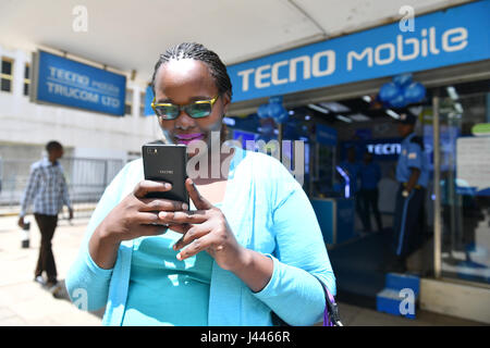 (170510) -- NAIROBI, May 10, 2017 (Xinhua) -- A woman uses Tecno mobile phone in front of a Tecno Mobile shop in downtown Nairobi, capital of Kenya, May 9, 2017. Chinese mobile phone manufacturer Tecno Mobile sales reached 25 million devices, including 9 million smartphones in 2015, helping it to sustain the most 'popular' brand status in Africa. (Xinhua/Sun Ruibo) (jmmn) Stock Photo