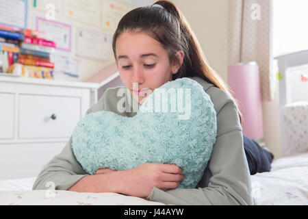 Young Girl Lying On Bed Hugging Heart Shaped Cushion Stock Photo