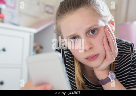 Young Girl Victim Of Bullying By Text Message Lying On Bed At Home Stock Photo
