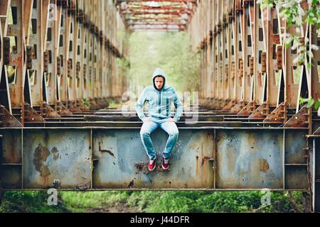 Sad man sitting on the abandoned rusty bridge. Concept for sadness, loneliness and more. Stock Photo