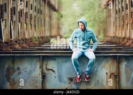 Sad man sitting on the abandoned rusty bridge. Concept for sadness, loneliness and more. Stock Photo