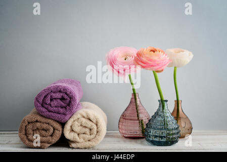 Folded towels with ranunculus in vases on blue background Stock Photo