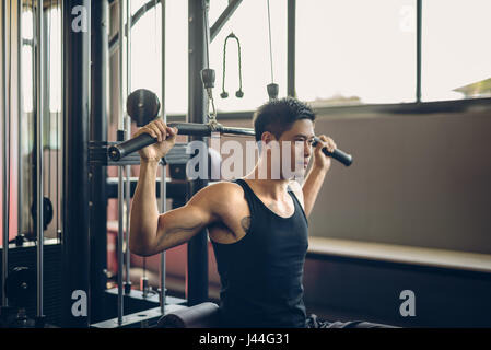 Asia Man with muscle in lat pull-down gym machine. Tough guy so strong muscle in the fitness gym. Stock Photo