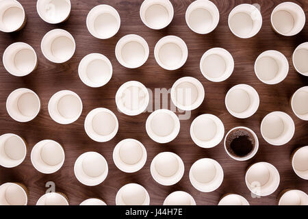 Looking down from above at lots of take away coffee cups on a wooden background all empty except one which has black coffee in it Stock Photo