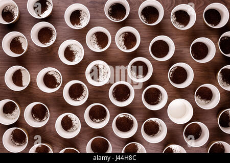 Looking down from above at lots of take away coffee cups on a wooden background all have coffee granules in them except one which is empty Stock Photo