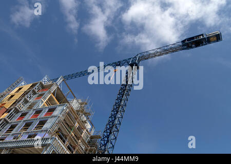 Different perspective looking up at a colorful building construction with a towering crane overhead against a blue sky and clouds Stock Photo
