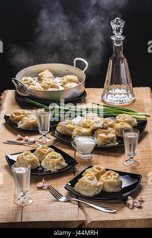 Ready hot manti on black plates, vodka in the countess and three piles on an oak table-top Stock Photo