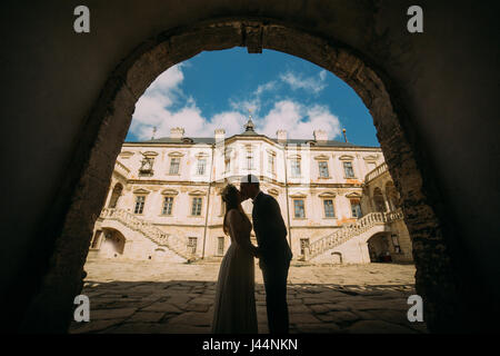 Passionate enloved couple share romantic at entrance arch of magnificent looking baroque palace shined by bright summer sun rays Stock Photo