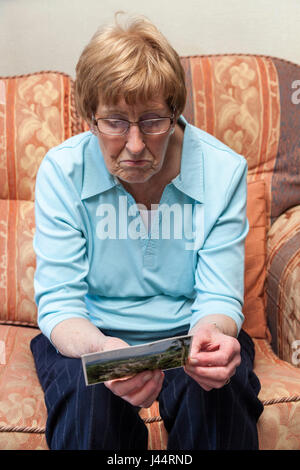 Older woman reading at a postcard and looking grumpy Stock Photo