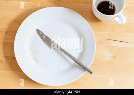 Finished eating. Leftovers; a plate with crumbs, a used knife and empty coffee cup after breakfast or mid morning snack Stock Photo
