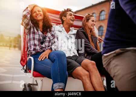 Cheerful teenage friends having fun on tricycle in the city. Young man and women riding on tricycle on road. Stock Photo