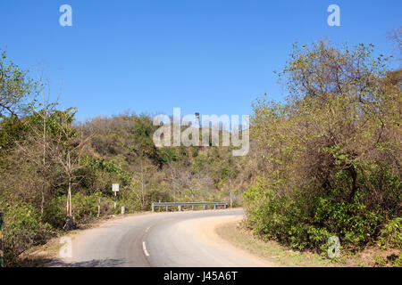 a bend in the morni hills mountain road with metal barriers going through sandy hillsides and acacia forest under a blue sky near chandigarh india Stock Photo