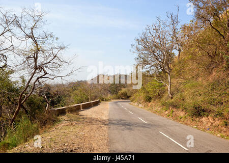 a scenic road going through the nature reserve of morni hills near chandigarh in india with sandy hills trees and forest under a cloudy blue sky in sp Stock Photo