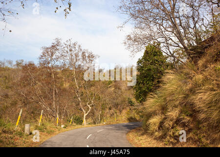 a bend in the Morni hills mountain road with marker posts going through sandy hillsides and acacia forest under a blue cloudy sky near chandigarh indi Stock Photo