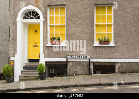 Exterior of British traditional house in Queens Parade, Bristol, UK. With grey walls, yellow front door and two windows with yellow curtains. Flowers  Stock Photo