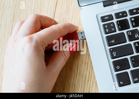 Close up of a woman hand plugging a red pendrive on a laptop Stock Photo