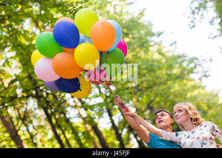 summer holidays, celebration and dating concept - couple with colorful balloons outdoors Stock Photo