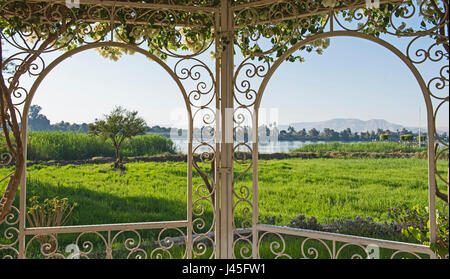 Scenic rural countryside landscape view of a large river in summer across meadow through metal trellis frame with bougainvillea