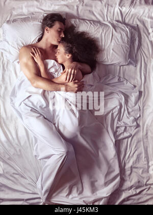 Couple sleeping together in an enbrace in bed in a bedroom lit by bright morning sunlight