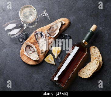 Opened oysters, ice and lemon and white wine on stone table. Top view Stock Photo