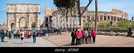 A 3 picture stitch panoramic exterior view at the entrance to the Colosseum with tourists visiting and taking group photographs on a sunny day. Stock Photo